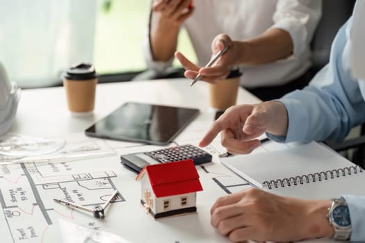 Two professionals engage in a detailed discussion about housing project plans, emphasizing teamwork as they analyze design aspects with a miniature house model.