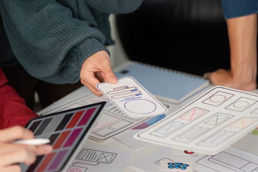 A team member presents a mobile layout prototype to colleagues, highlighting the design elements on a conference table filled with sketches and digital inspirations.