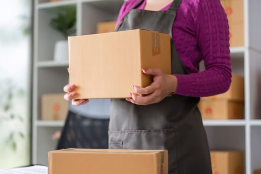 An online seller carefully holds a cardboard box, getting ready to pack items for shipment. The workspace reflects an organized and efficient logistics environment.