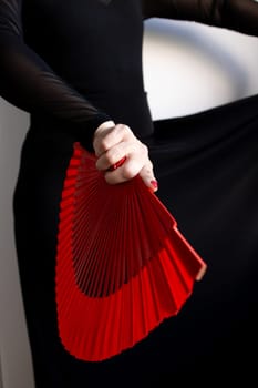 Elegant female holding red fan in black attire.
