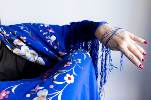 Elegant female arm in floral blue shawl with fringe details.
