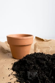 Empty terracotta pot with soil on craft paper against white background.