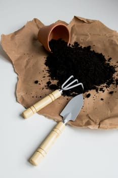 Brown paper with spilled soil and gardening tools on white background.