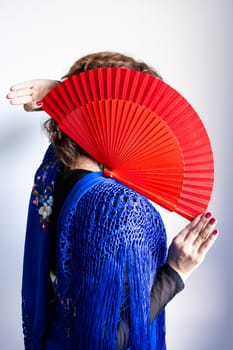 Female in traditional spanish attire with red fan covering face.
