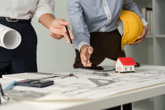 In a collaborative setting, architects discuss project details while referencing blueprints and tools, emphasizing teamwork and effective planning.