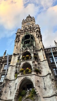 10.10.2024 Munich, Germany - New Town Hall Tower, Rathaus. 10.10.2024 Munich, Germany - New Town Hall Tower. A low-angle view of the New Town Hall (Neues Rathaus) in Munich, Germany. The historic Gothic Revival-style tower features intricate architectural details, a famous Glockenspiel, and decorative flowers adorning the balconies. The sky is a blend of blue and soft clouds, enhancing the grand appearance of this iconic landmark.