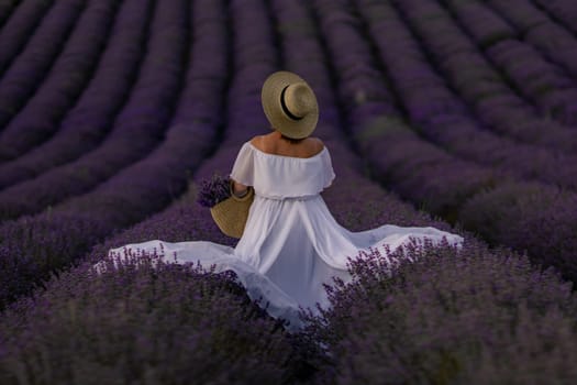 Here's a caption under 150 characters describing the image: Woman in white dress and straw hat stands amidst rows of blooming purple lavender, holding a basket of flowers. Serene lavender field scene.
