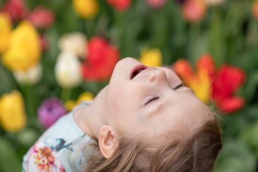 Happy girl laughs in a park with the tulips