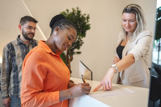 A woman is standing at a desk, signing a piece of paper. She appears focused as she carefully puts pen to paper, possibly completing an important document or contract. The scene conveys a sense of professionalism and responsibility.