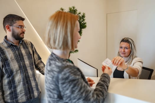 A woman extends her hand holding a piece of paper towards a man, who is attentively looking at the document. The scene captures a moment of communication and exchange between the two individuals.