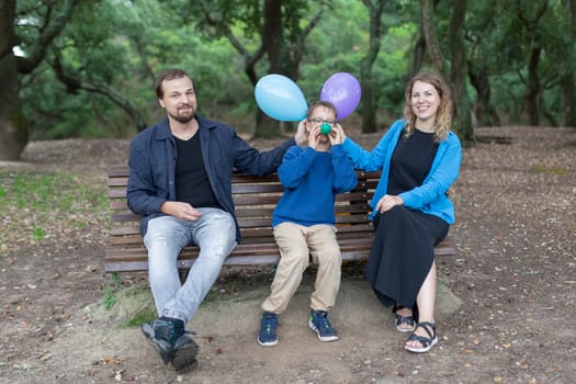 Smiling family having fun with colorful balloons while sitting on a bench in a park