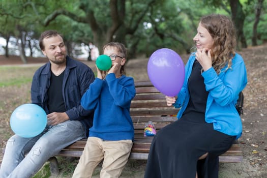 Smiling family inflating colorful balloons while sitting on a park bench