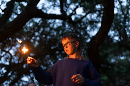 Young boy holding sparkling bengal light in the woods at dusk