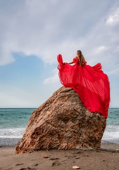 woman sea red dress. Woman with long hair on a sunny seashore in a red flowing dress, back view, silk fabric waving in the wind. Against the backdrop of the blue sky and mountains on the seashore