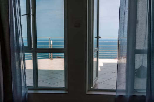Open window frames a sea view with curtains, leading to a balcony and ocean horizon.
