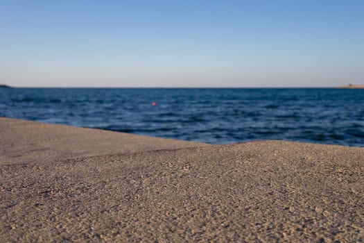 A sandy beach stretches towards a calm, blue ocean under a clear sky. The water gently laps at the shore, creating small waves.