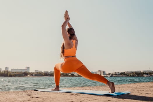 A woman in an orange outfit performs a yoga pose on a blue mat by a body of water. The sun is shining brightly in the background.