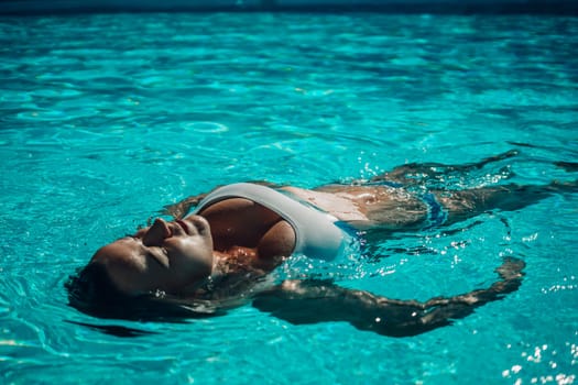 Woman relaxing swimming pool. Happy woman in a blue swimsuit floating in the pool, look form above.