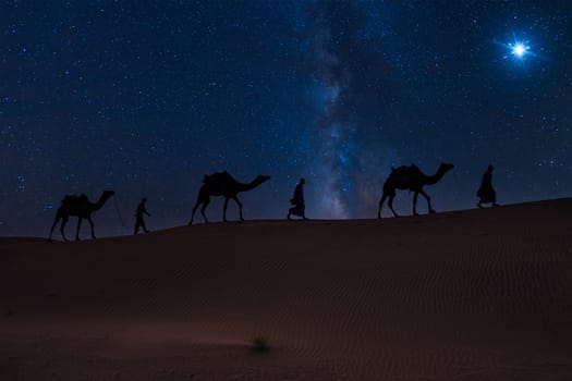 Christmas Jesus birth concept - Adoration of the Magi, Three Wise Men, Three Kings, and the Three biblical Magi with camel silhouettes journeying in sand dunes of desert follow Bethlehem star at night