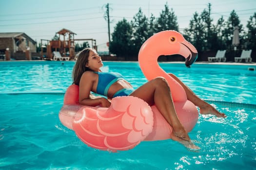 A woman is floating on a pink flamingo float in a pool. The scene is relaxed and fun, with the woman enjoying her time in the water