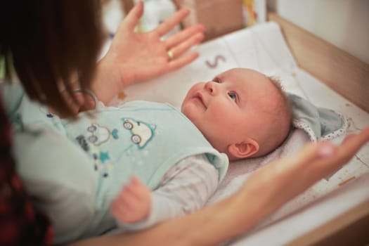 4 months old infant baby boy at changing table, mother playing with him, detail from above