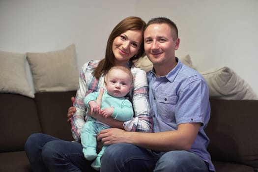 Young couple sitting on couch with his 3 months old baby boy, posing for family photo