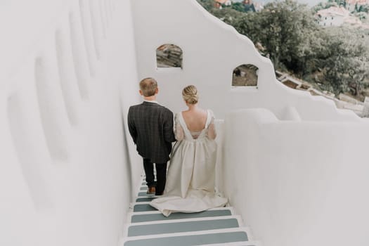 A bride and groom are walking down a white staircase. The bride is wearing a white dress and the groom is wearing a suit