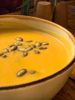 Creamy pumpkin soup with pumpkin seeds in a ceramic bowl on a wooden table. Photo taken with a smartphone.