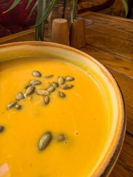 Creamy pumpkin soup with pumpkin seeds in a ceramic bowl on a wooden table. Photo taken with a smartphone.