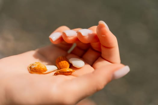 A person is holding a handful of nuts in their hand. The nuts are of different sizes and shapes, and they appear to be almonds. The person seems to be enjoying the nuts and is likely to eat them soon