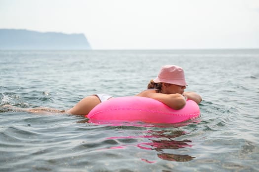 A woman is laying on a pink inflatable raft in the ocean. The scene is peaceful and relaxing, with the woman enjoying the water and the sun