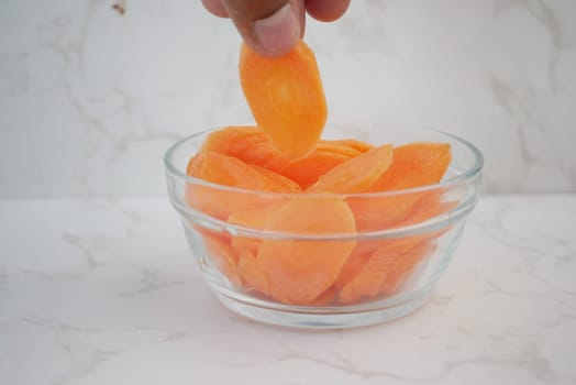 Fresh carrot slices are being lifted from a clear glass bowl.