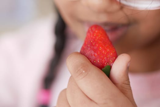 A child holds a ripe strawberry close to her mouth, excited to eat.