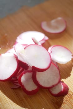 Bright red radish slices are arranged on a cutting board in sunlight.