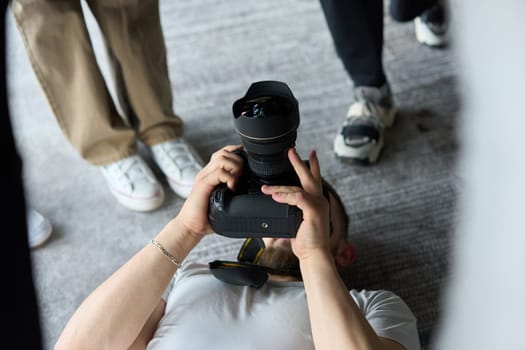 A photographer lies on the floor, capturing a heartfelt shot of a group of models embracing each other, showcasing their natural connection and joy in an intimate and creative moment.