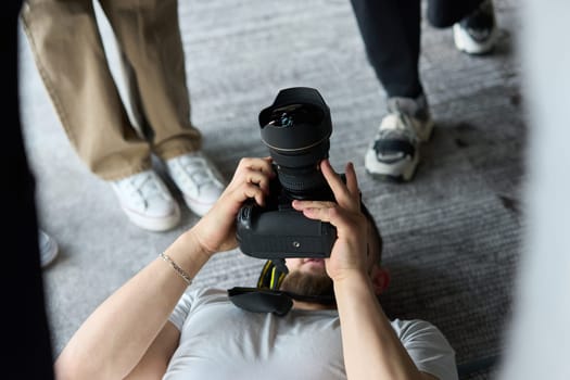 A photographer lies on the floor, capturing a heartfelt shot of a group of models embracing each other, showcasing their natural connection and joy in an intimate and creative moment.