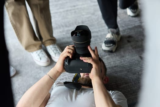 A photographer lies on the floor, capturing a heartfelt shot of a group of models embracing each other, showcasing their natural connection and joy in an intimate and creative moment.
