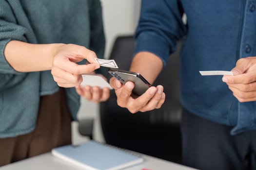 Hands of team members exchange design prototypes while engaging with digital devices, emphasizing the collaborative spirit in their creative process.