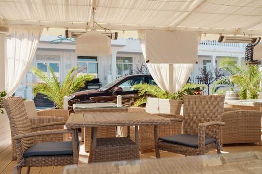 Wicker furniture tables in the open air are waiting for visitors. The interior of the restaurant in the open air. Empty tables of street cafe