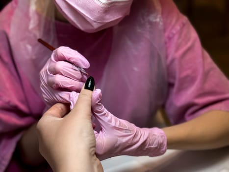 Asian female applying black nail polish in salon setting.