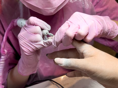 Female manicurist performing pink acrylic nail filing in close up.