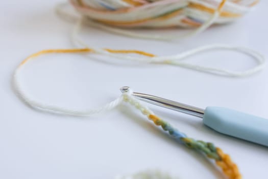 Close up of crochet hook and multicolored yarn on white background.