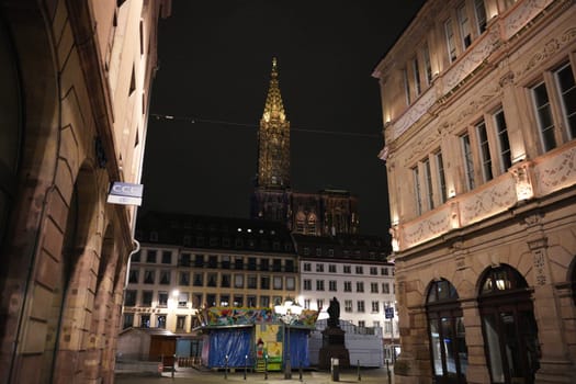 View of Strasbourg Cathedral illuminated at night, seen from a quiet city square surrounded by classic French buildings and closed stalls.