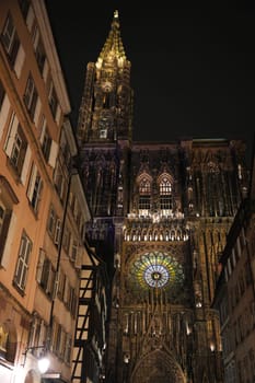 Vertical view of Strasbourg Cathedral illuminated gothic facade, towering spire, and radiant rose window framed by traditional buildings.