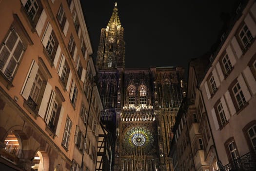 Breathtaking night view of Strasbourg Cathedral ornate fasade and glowing rose window, framed by surrounding traditional buildings