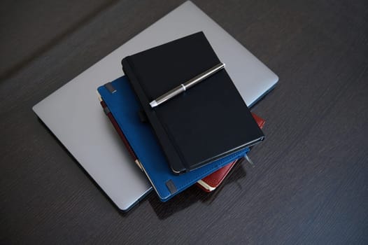A neat arrangement of a laptop and several notebooks creates an atmosphere of productivity. The wooden desk adds warmth to the organized workspace. Perfect for business or creative projects.