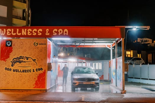 Serviceman at a car wash stands next to the car in a thick water spray. High quality photo