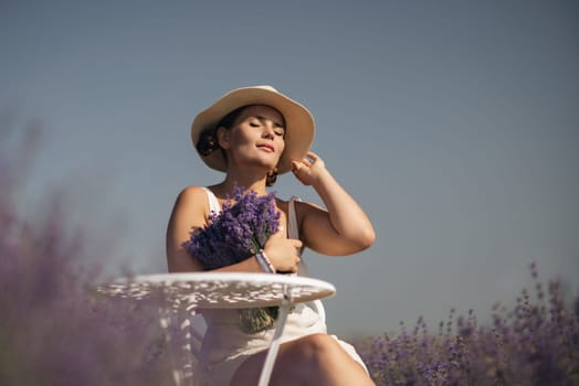 A woman is sitting in a field of lavender flowers and wearing a straw hat. She is smiling and holding a bouquet of flowers. Scene is peaceful and serene, as the woman is surrounded by the beauty of nature.