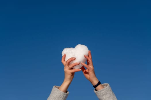 Two hands hold a white heart-shaped object aloft against a vibrant blue sky.