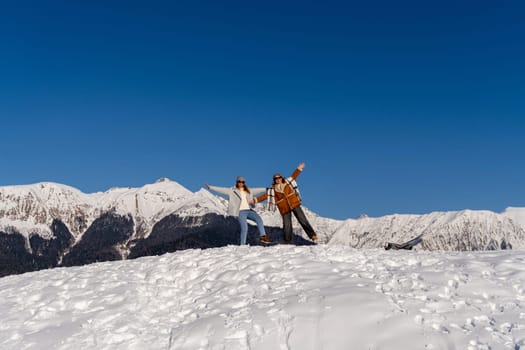 Two people joyfully celebrate atop a snow-covered mountain ridge under a vibrant blue sky. A breathtaking winter landscape.